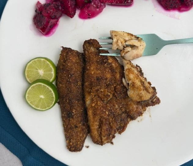 Crispy pan-fried perch fillets on a plate with lime wedges, showing the flaky white flesh inside