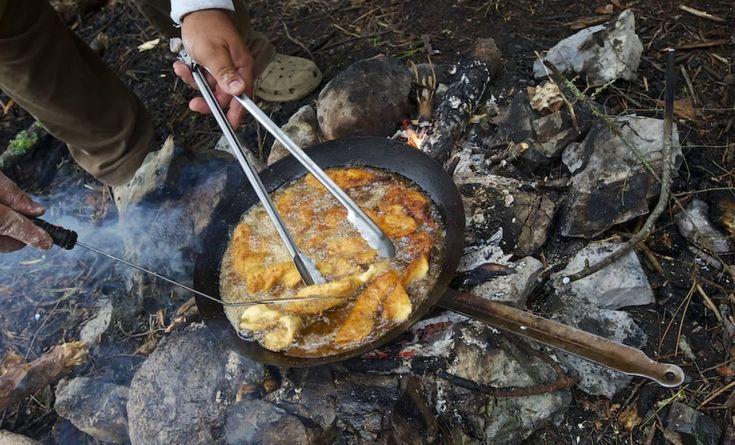 Fish frying in a pan over a campfire on the rocks